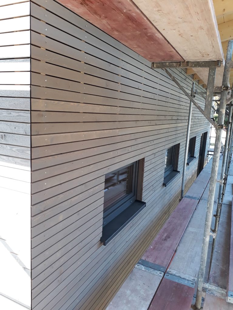 Holzrahmenbau-Aufstockung eines Büro- und Lagergebäudes  mit aufgeständertem Treppenpodest und einer waagerechten Rhombusleisten-Fassade in sibirischer Lärche